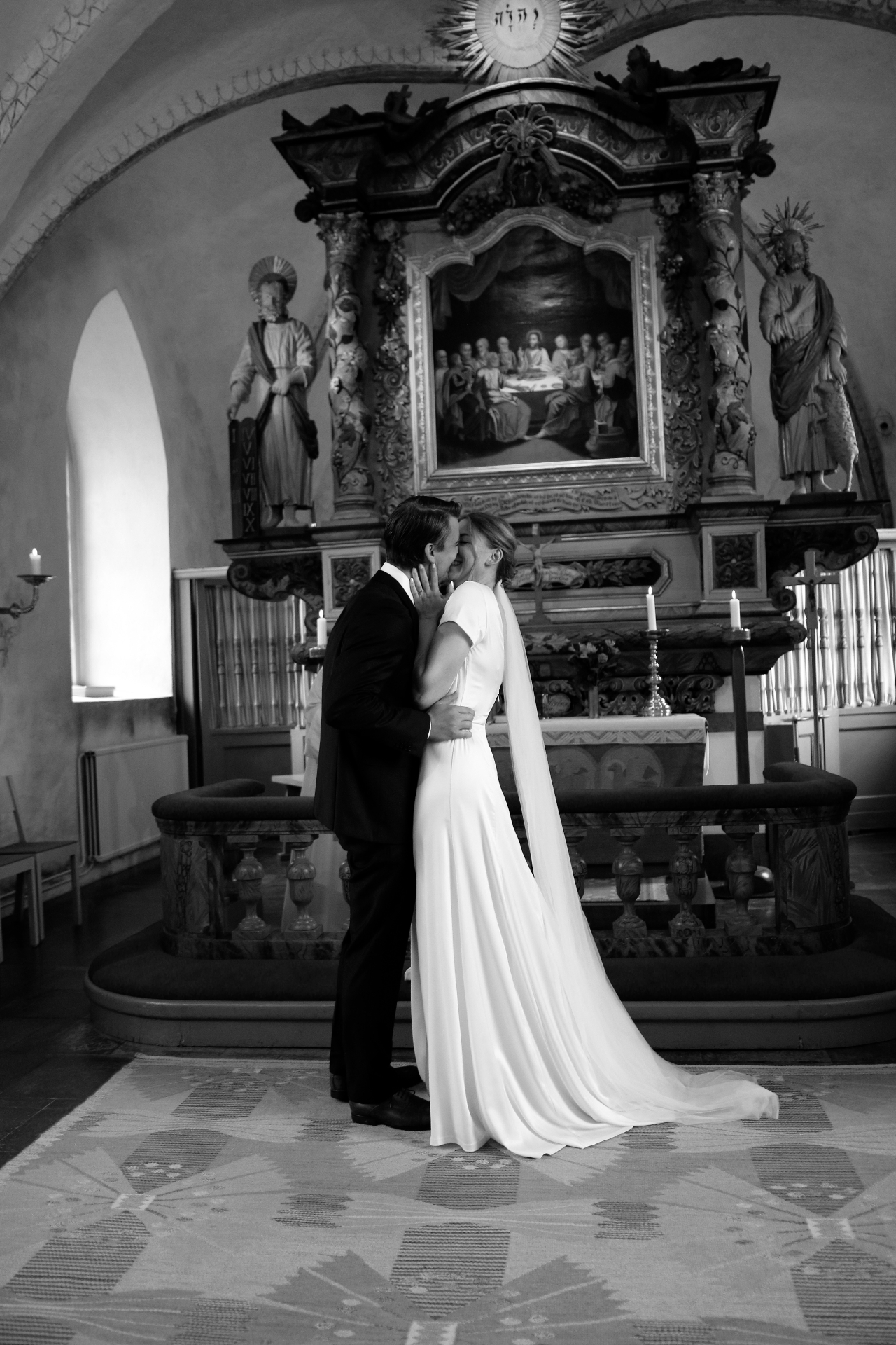 Brudpar kysser varandra framför altartavla i kyrka — svartvitt