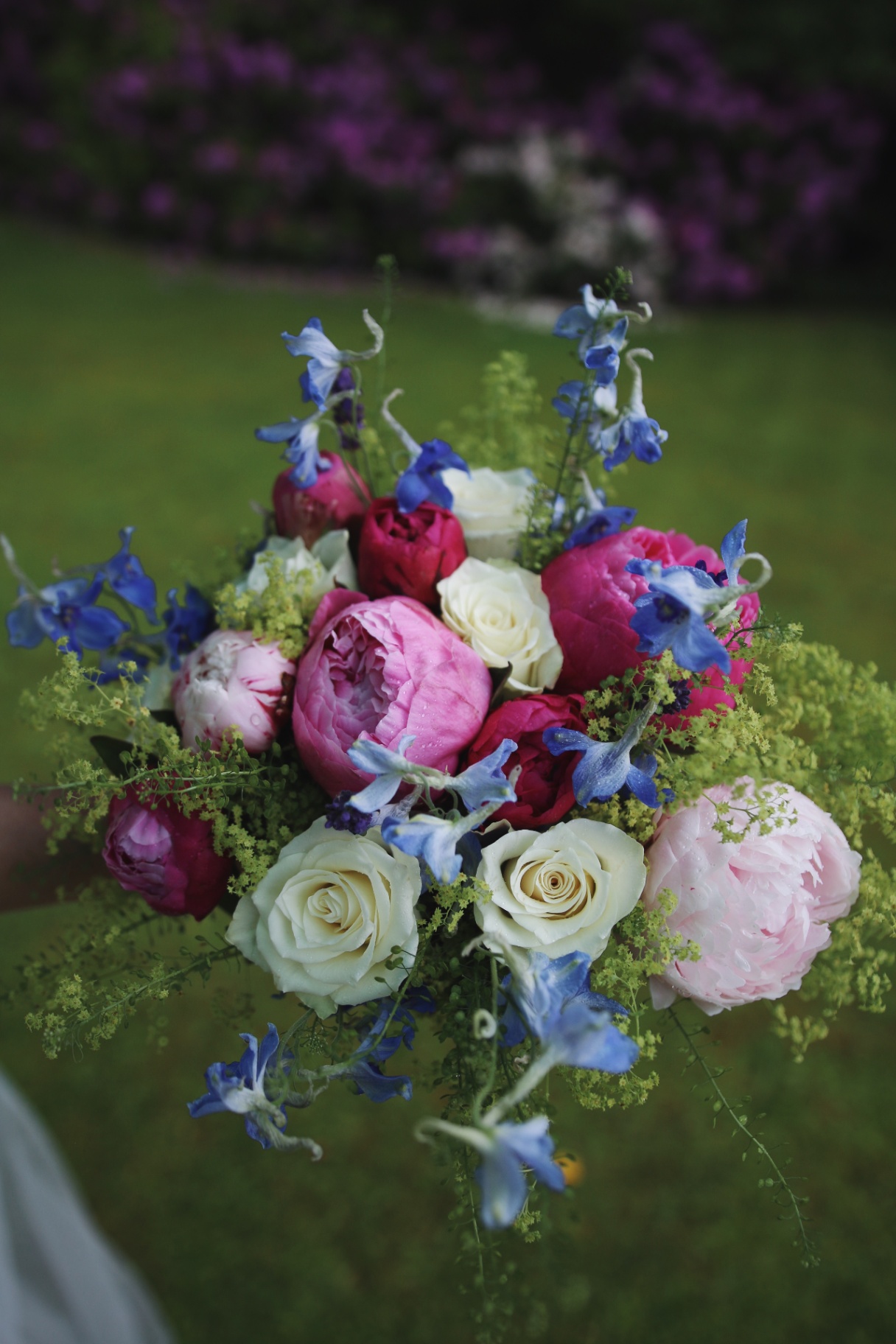 Brudbukett med pioner, rosor och blå delphinium i trädgård