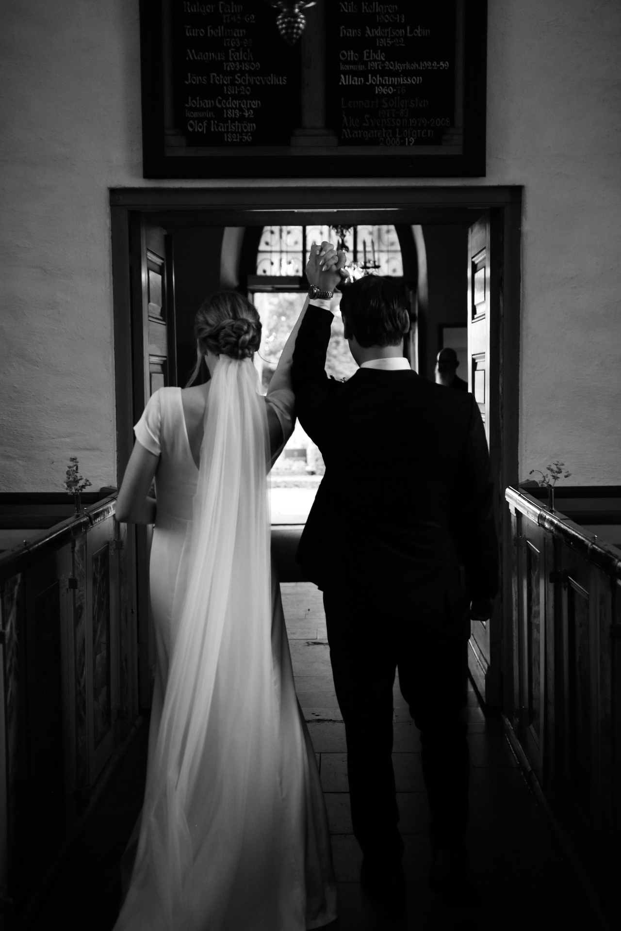Brudpar går ut ur kyrkan med upplyfta händer — svartvitt
